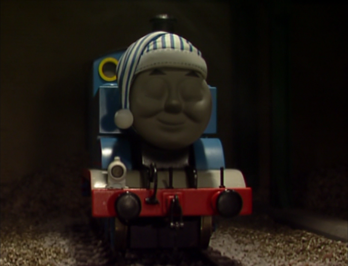 thomas the tank engine in a kind of dark setting, with shut eyes and a smile, looking like he's asleep (in one of those sleeping hats as well)